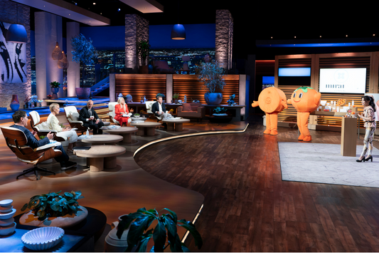 Koko presenting on Shark Tank with two persimmon mascots in front of the panel of investors.