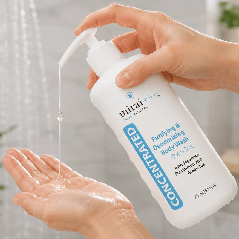 A hand holds a white pump bottle of mirai CLINICAL Purifying & Deodorizing Body Wash, with a clear stream of gel being dispensed into the other hand against a softly blurred bathroom background.