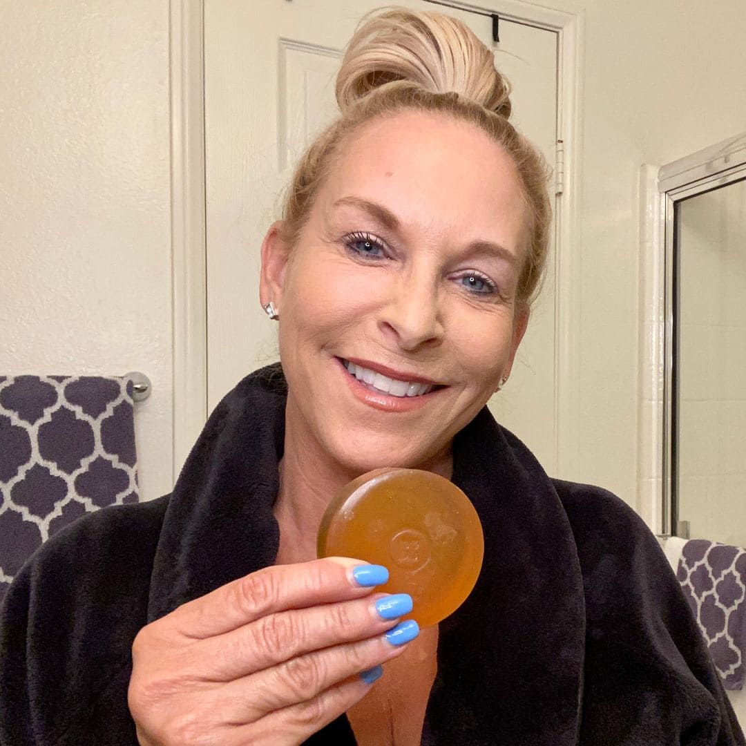 Smiling woman in a black robe holding Mirai Clinical persimmon soap in bathroom, showcasing natural deodorizing bar for aging odor and daily freshness.