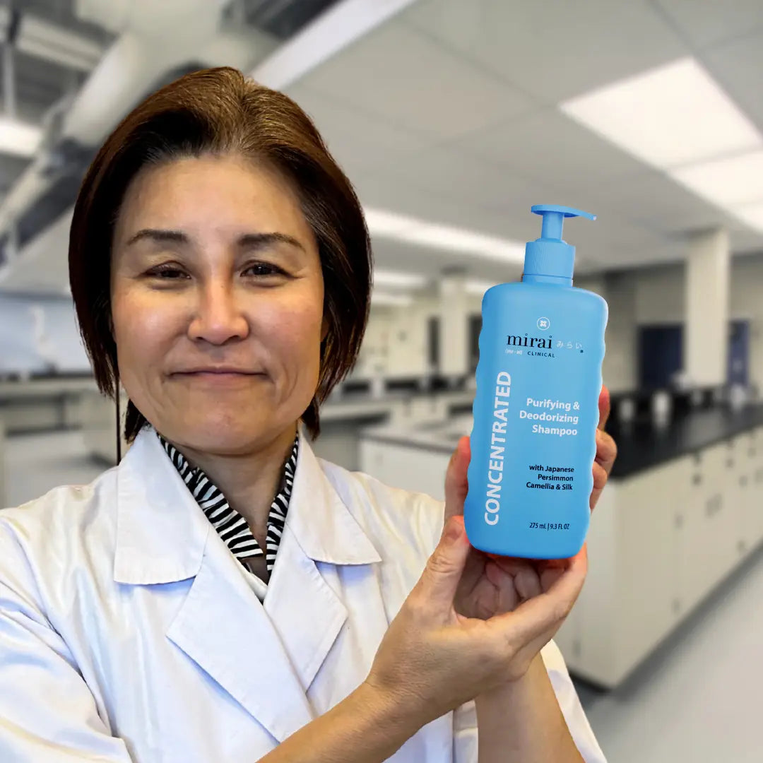 Dr. Yoko holding Mirai Clinical Purifying & Deodorizing Shampoo with Japanese Persimmon, Camellia, and Silk in a laboratory setting.