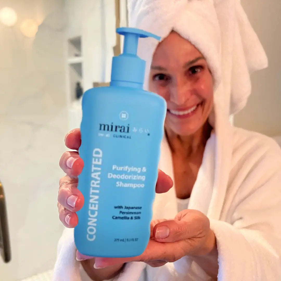Mirai Clinical Purifying & Deodorizing Shampoo with Japanese Persimmon, Camellia, and Silk, held by a woman wrapped in a towel.