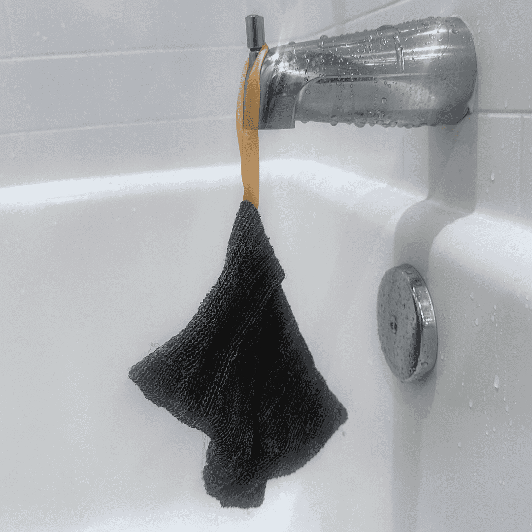 Mirai Clinical Soap Saver Scrub Bag hanging on a bathtub faucet for drying.
