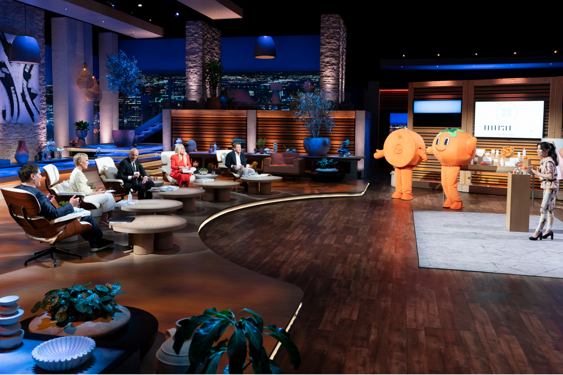 Koko presenting on Shark Tank with two persimmon mascots in front of the panel of investors.