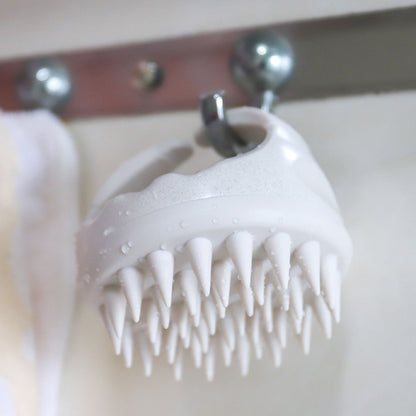 Mirai Clinical Scalp Massager hanging, showcasing its ergonomic design and silicone bristles.