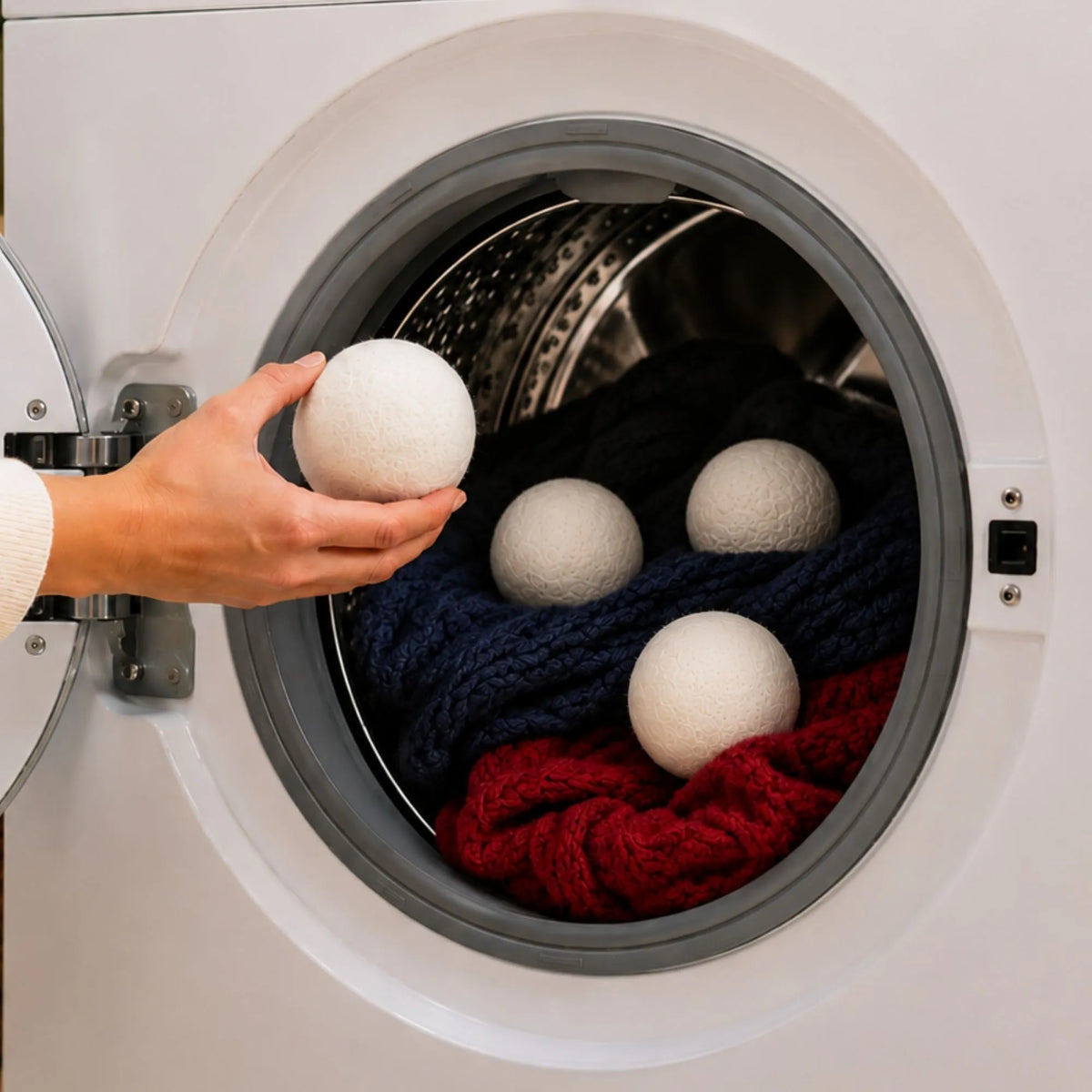 Hand placing reusable wool dryer balls into a clothes dryer to improve airflow, soften fabrics, and shorten drying time.