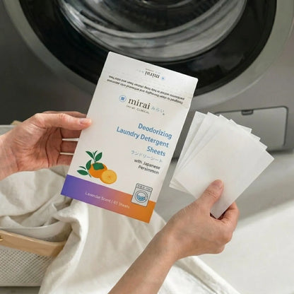 Hands holding Mirai Clinical deodorizing laundry detergent sheets with persimmon extract in front of a washing machine for removing body and aging odor from clothes.