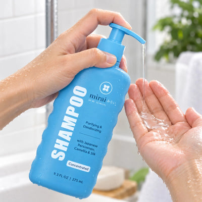 Hand pumping Mirai Clinical Purifying & Deodorizing Shampoo with Japanese Persimmon, Camellia & Silk into an open palm in a bright bathroom.