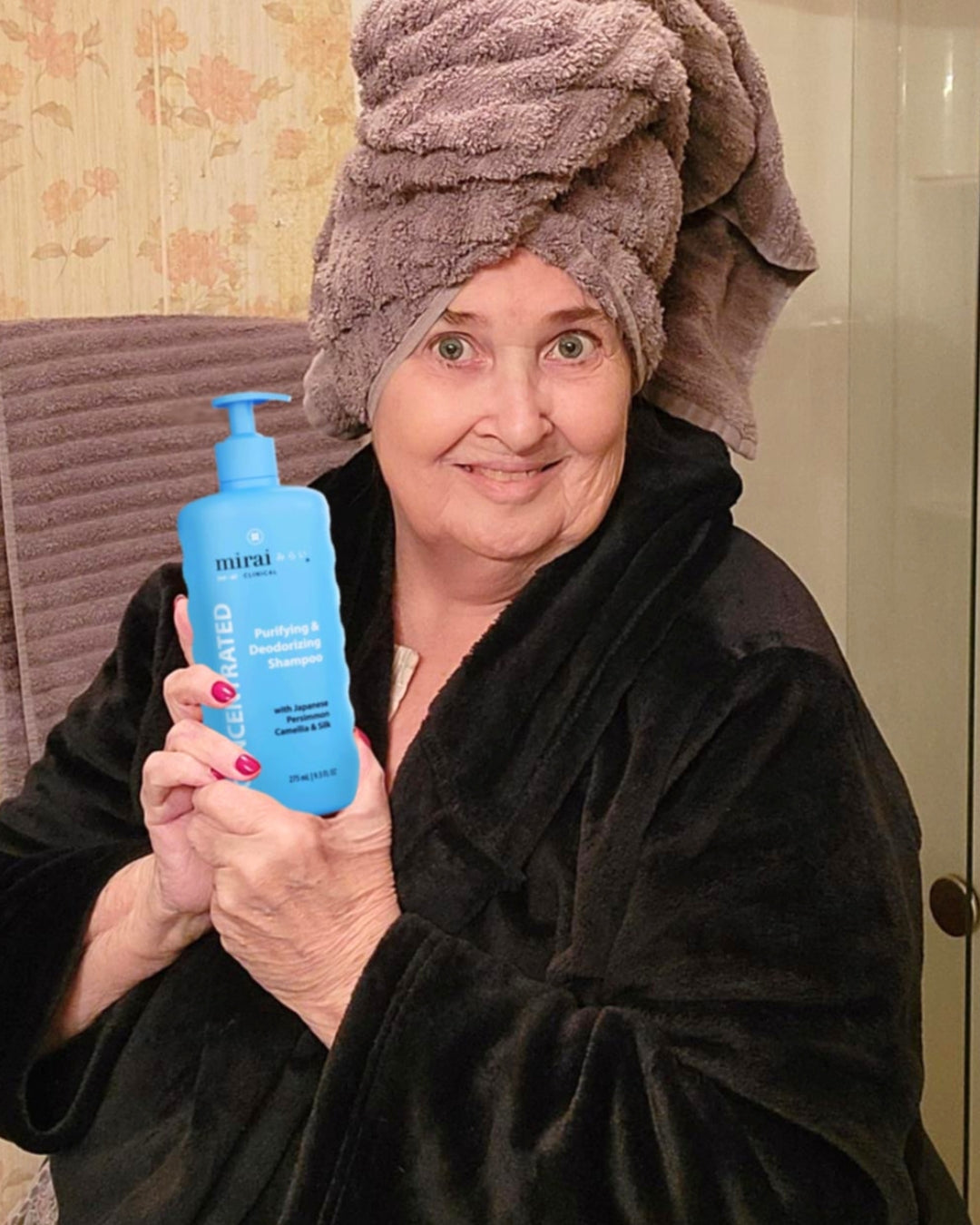 Woman in a bathrobe holding Mirai Clinical purifying and deodorizing hair shampoo with persimmon