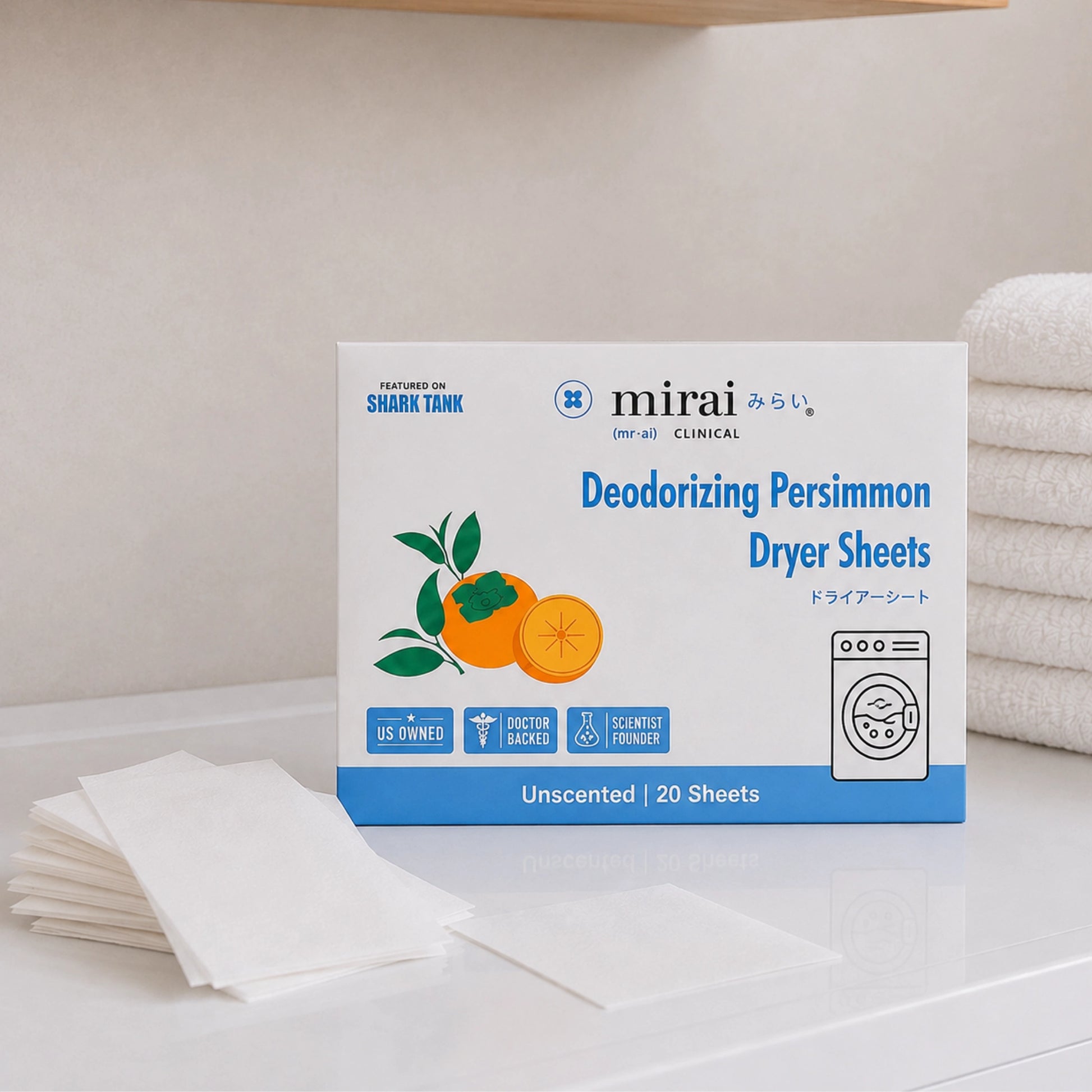 A box of Mirai Clinical Deodorizing Persimmon Dryer Sheets stands on a white countertop with a stack of white dryer sheets in front and folded white towels in the background.