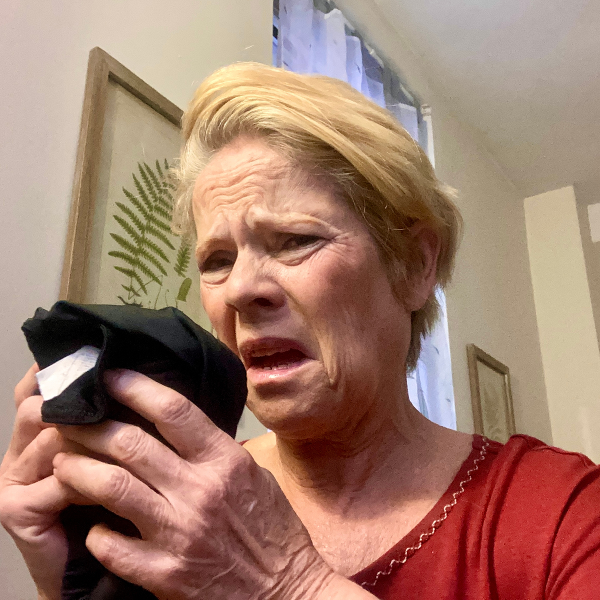 Mature woman grimacing while smelling a black shirt, noticing the lingering odor caused by Nonenal aging body odor