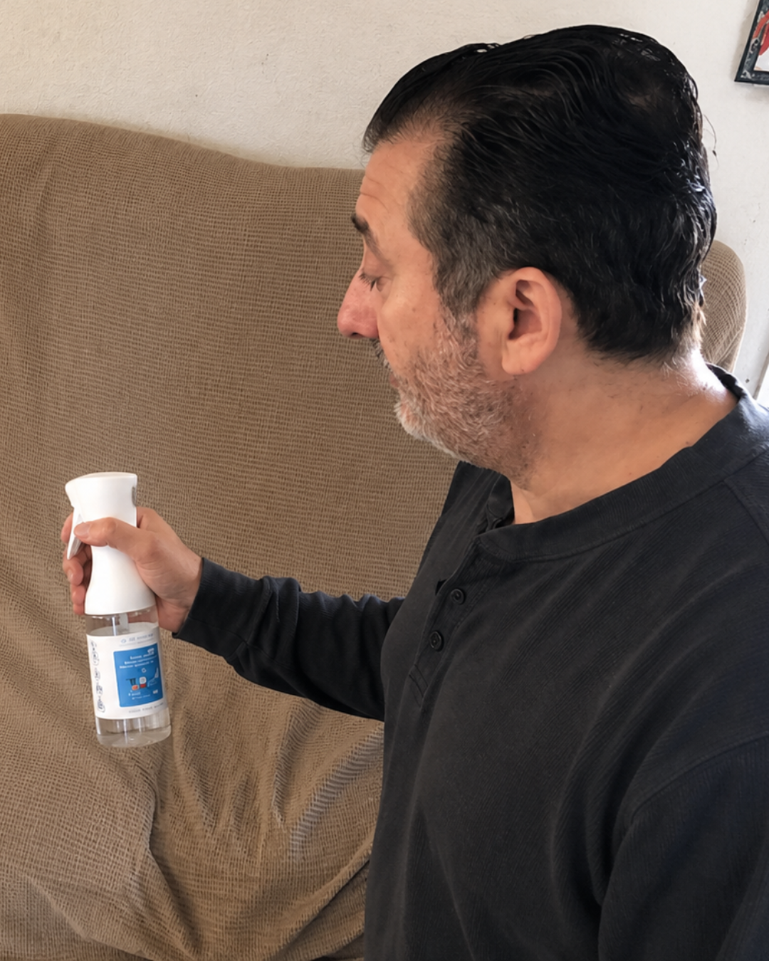 Man using Mirai Clinical deodorizing room spray on a couch to eliminate nonenal odors, refresh upholstery, and keep furniture smelling clean and fresh longer.