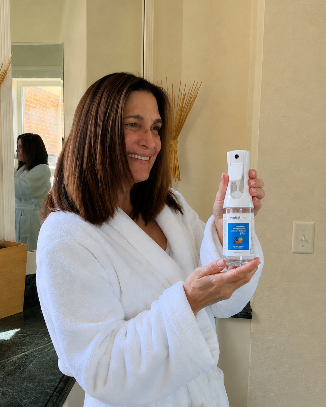 Woman holding Mirai Clinical deodorizing room spray to eliminate nonenal odors, freshen rooms, fabrics, and furniture for a clean, long-lasting scent.