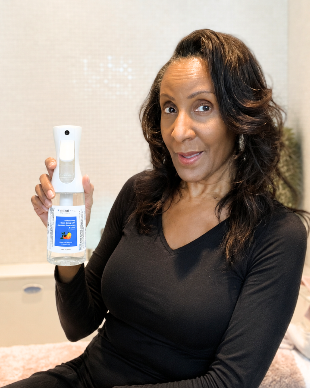 Woman holding Mirai Clinical deodorizing room spray for nonenal odor removal, helping eliminate aging odors and keep rooms, furniture, and fabrics smelling fresh.