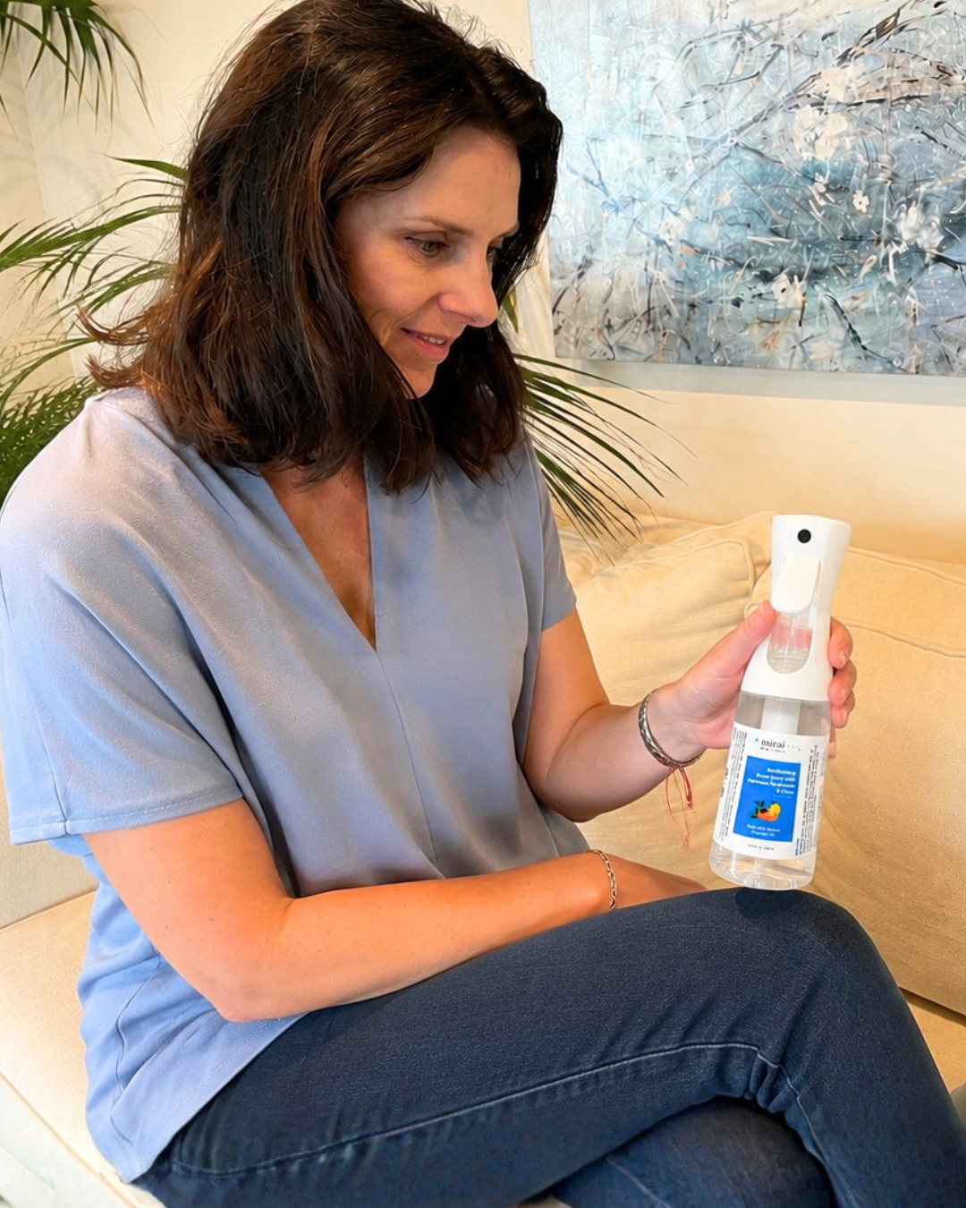 Woman holding Mirai Clinical deodorizing room spray to eliminate nonenal odors, freshen furniture and fabrics, and keep living spaces smelling clean.
